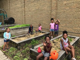 A group of smiling children play in raised garden beds